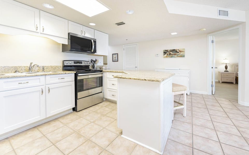 Bright kitchen features white cabinetry, granite countertops, and a breakfast bar with seating, leading to a cozy living area