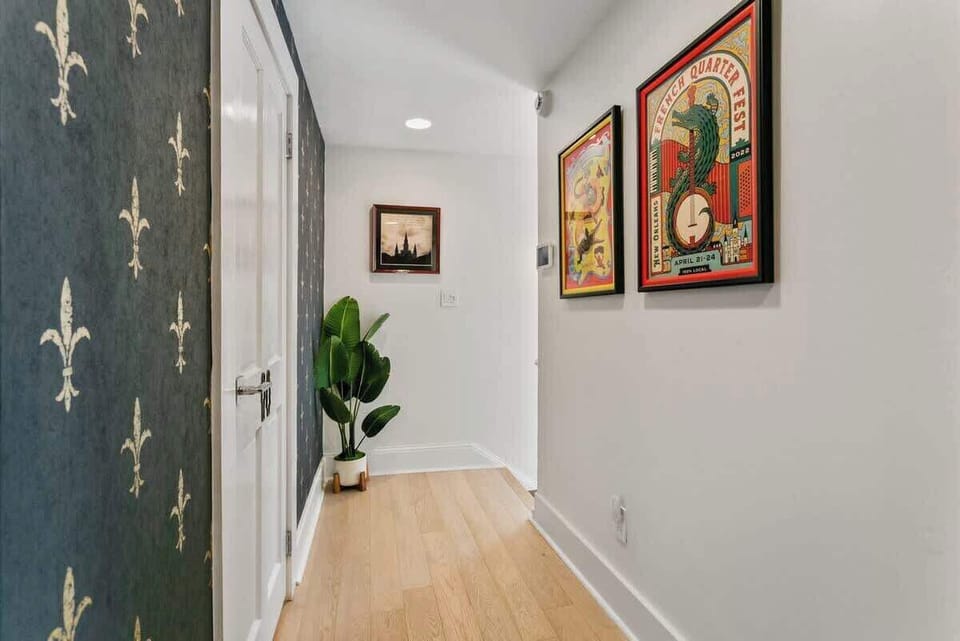 Hallway leading to the bathroom (left) and stairway exit, featuring bold fleur-de-lis wallpaper and local festival art. A stylish touch of New Orleans character as you move through the space.