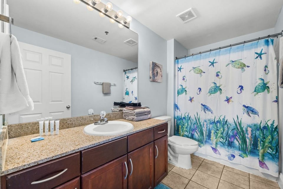 Freshen up in this bright bathroom with a granite vanity, large mirror, toilet, tub-shower combination, and colorful sea-life curtain.