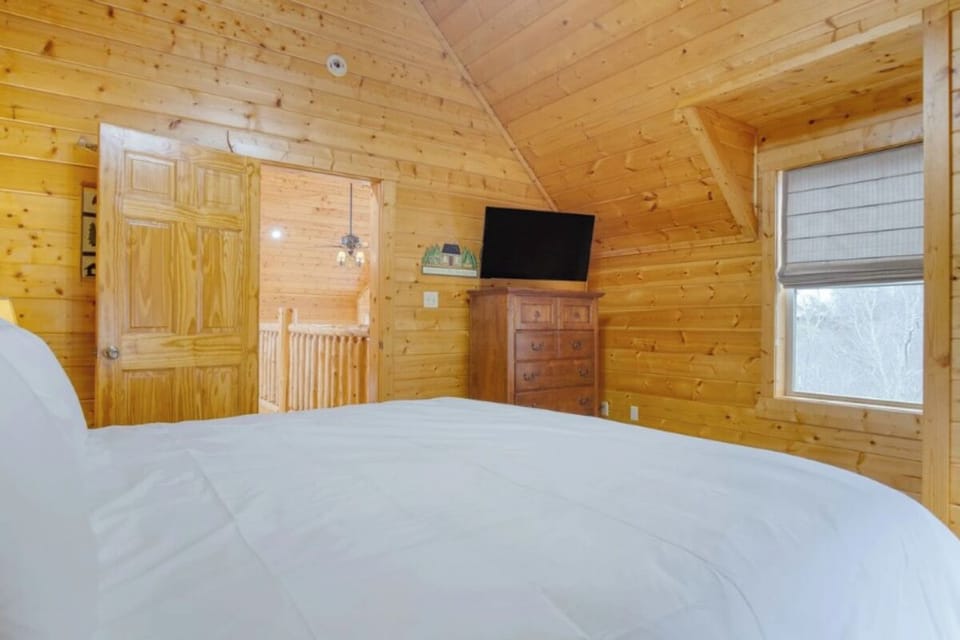 Cozy cabin bedroom with warm wood walls, crisp linens, and your own TV for relaxing mountain retreats.