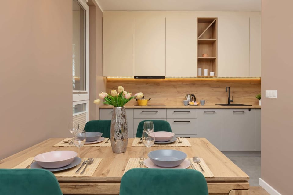 A modern dining area adjacent to the kitchen, featuring wooden accents and green chairs.
