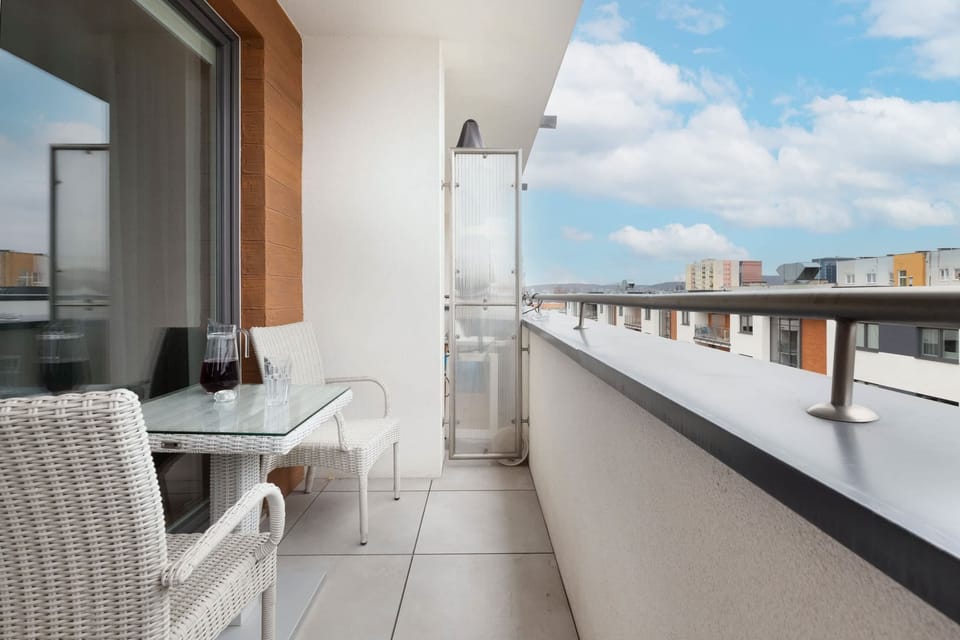 A modern balcony overlooking the urban skyline, perfect for enjoying a morning coffee. Glass railings provide an unobstructed view.