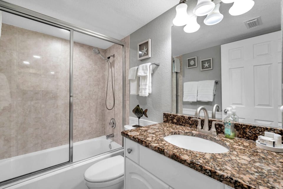 Bathroom w/ granite vanity, sink, & a shower & tub combo.