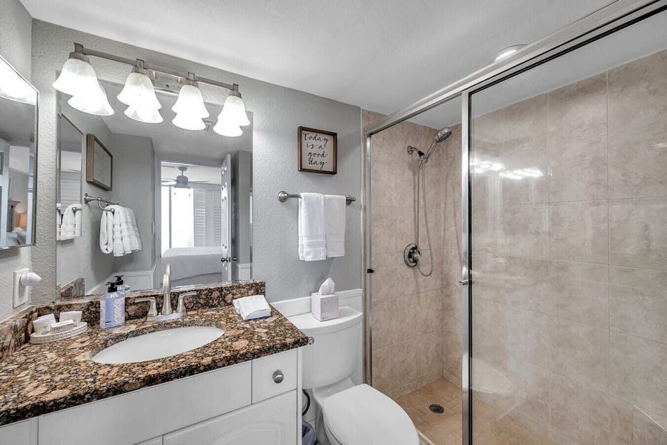 Clean bathroom w/ a glass-enclosed tub & shower combo and a spacious vanity area.