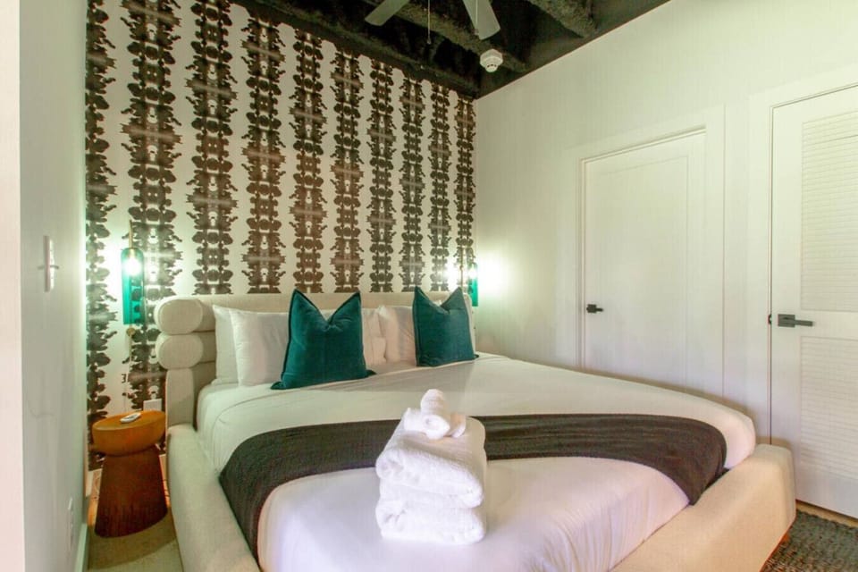 Bedroom featuring dramatic patterned wallpaper and crisp white bedding accented with rich teal pillows