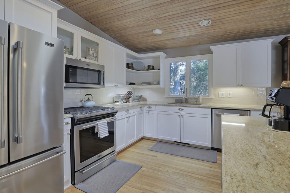 White kitchen cabinets with wood ceiling and floors, stainless steel appliances and a window over the sink.