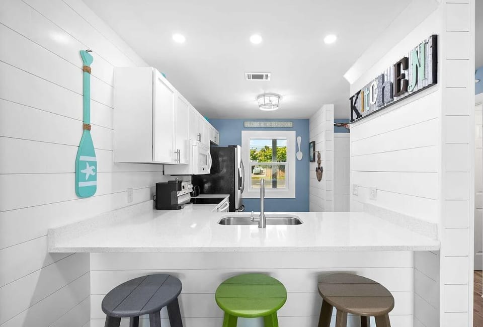 Modern kitchen with a white countertop and colorful bar stools.