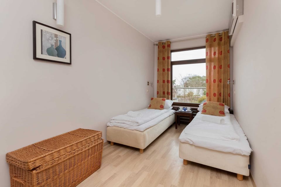 A simple bedroom featuring two single beds, a small bedside table, and a woven basket for storage.