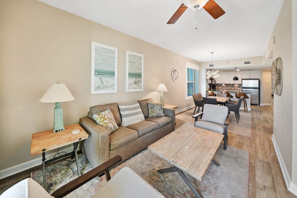 Unwind in your bright, modern living space with comfortable seating, coastal artwork, and open kitchen perfect for vacation relaxation.
