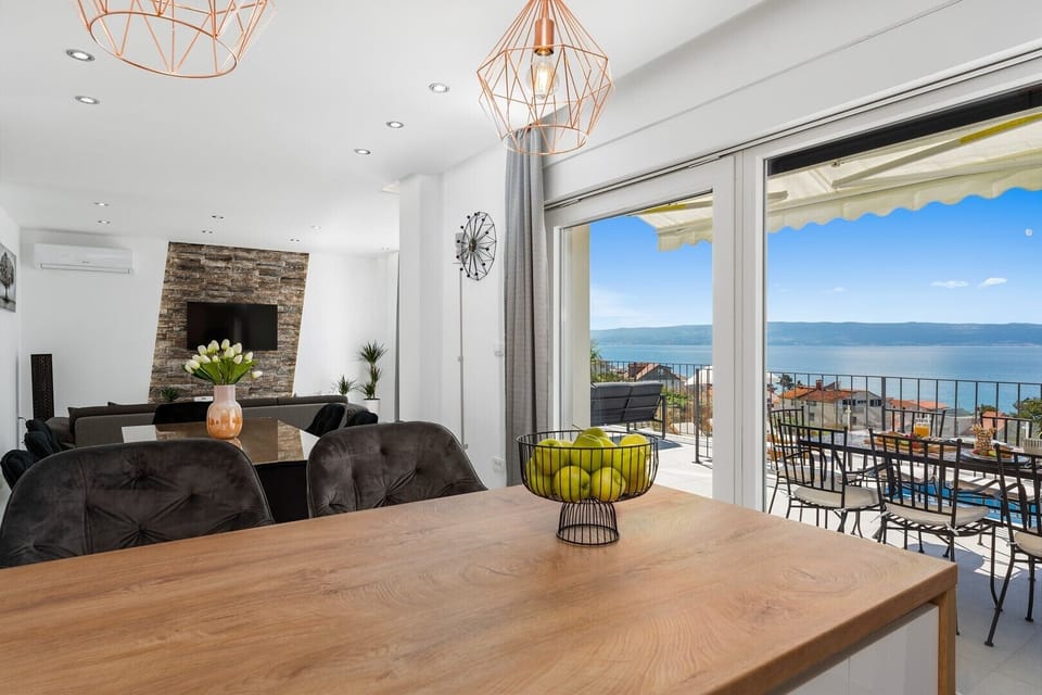 The living area is connected by an outdoor dining area and the pool area by glass floor-to-ceiling doors.
