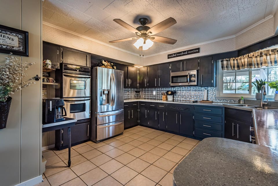 Tile flooring anchors the kitchen with black cabinetry, stainless steel appliances, and a ceiling fan overhead.