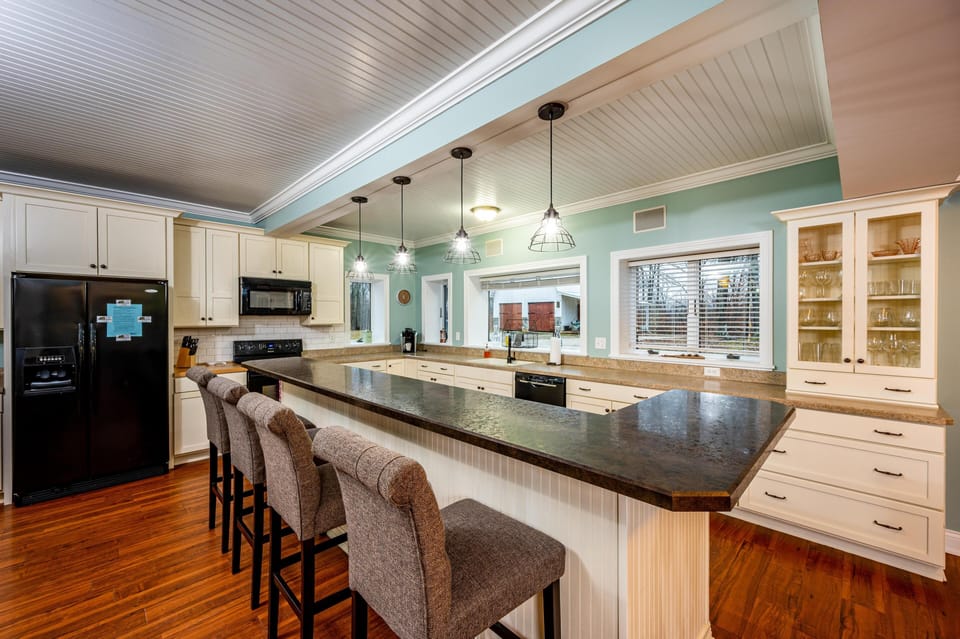 Four metal cage pendant lights illuminate the black granite countertop and soft green walls in the kitchen.
