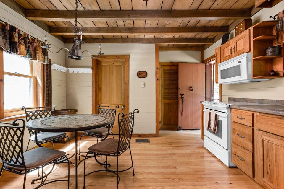 Living room dining area with wrought-iron chairs, mosaic round table, exposed wood beams, and hardwood floors.