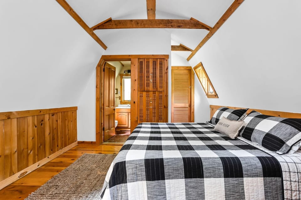 Upstairs bedroom with black-and-white plaid bedding, pine wood paneling, exposed ceiling beams, and an en suite bathroom.