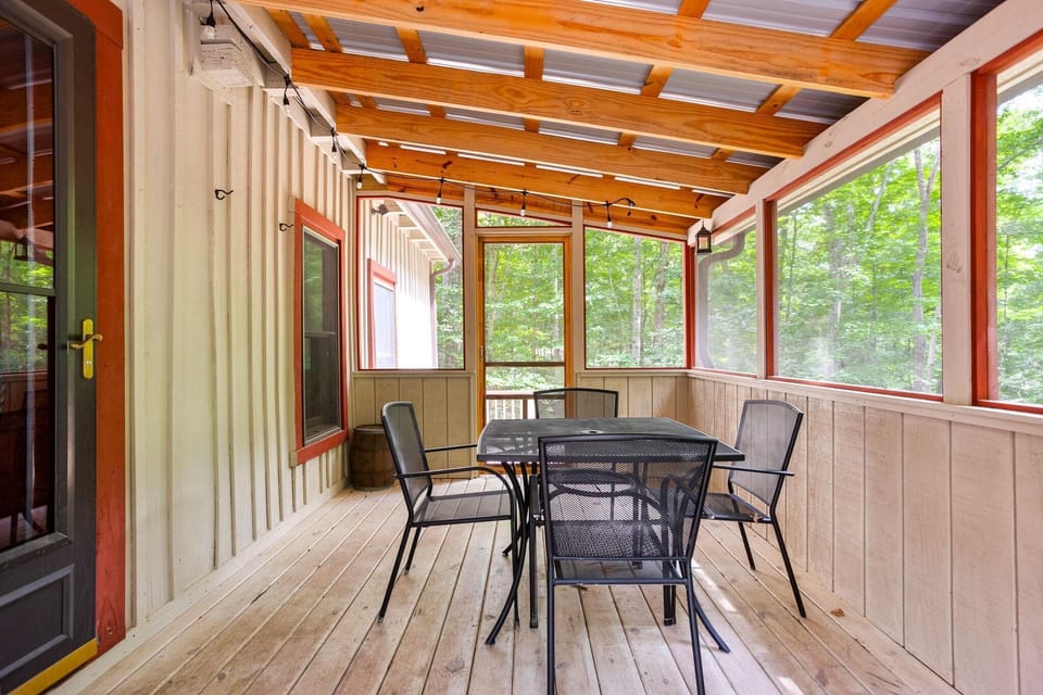 Screened porch with wood plank flooring, exposed rafters, red-trimmed windows, and black metal dining set.