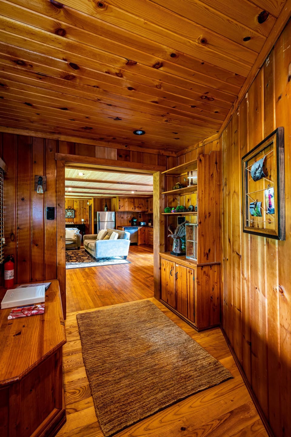 Entryway with honey-toned wood paneling, built-in shelving, and a textured beige rug leading to the living area.