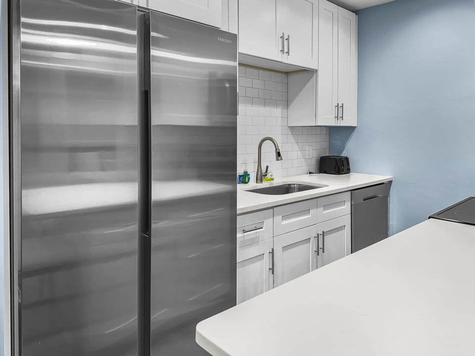 Kitchen with stainless steel refrigerator, white shaker cabinets, and dark countertops