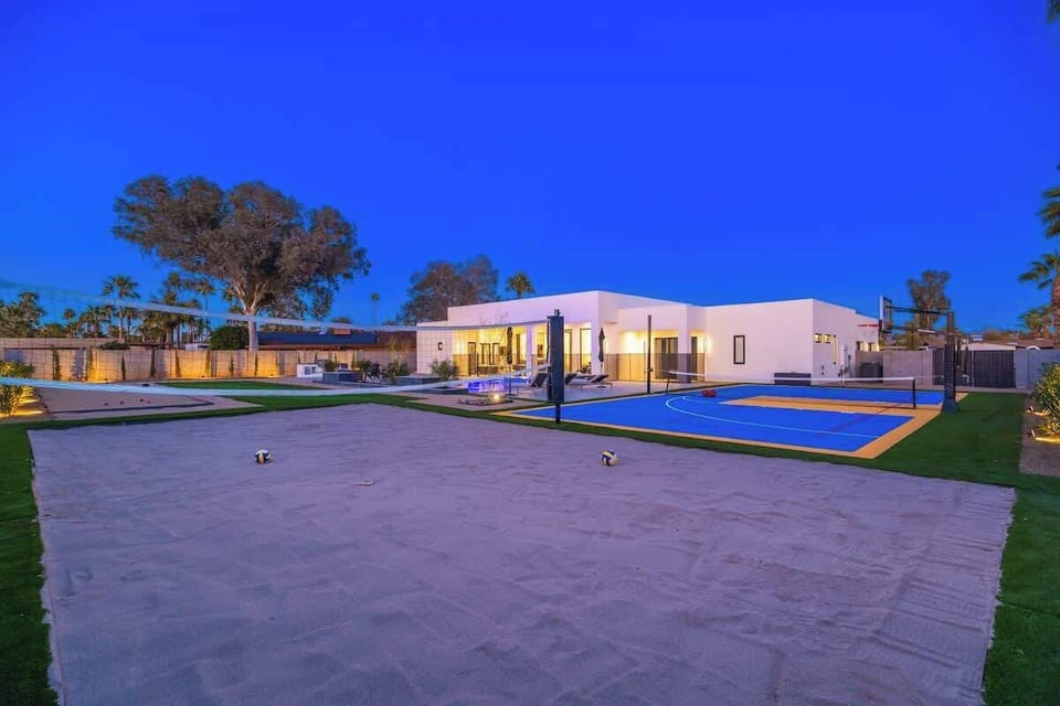 Modern desert estate with sparkling pool and basketball court under dramatic twilight sky, offering luxury amenities for recreation and relaxation.