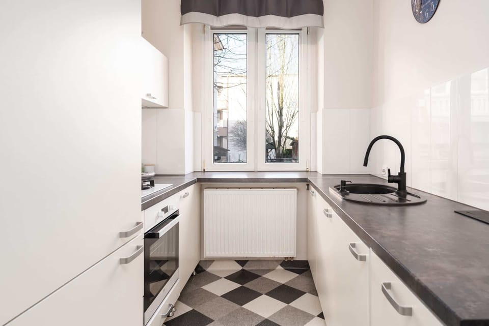A modern kitchen with white cabinets, a black countertop, and a black-and-white checkerboard-patterned floor.