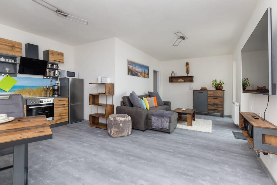 A modern living room featuring a flat-screen TV, wooden storage units, and comfortable gray furniture.