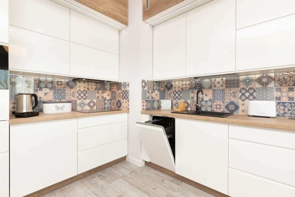 A modern white kitchen with sleek cabinets and patterned backsplash tiles. The space is clean and bright.