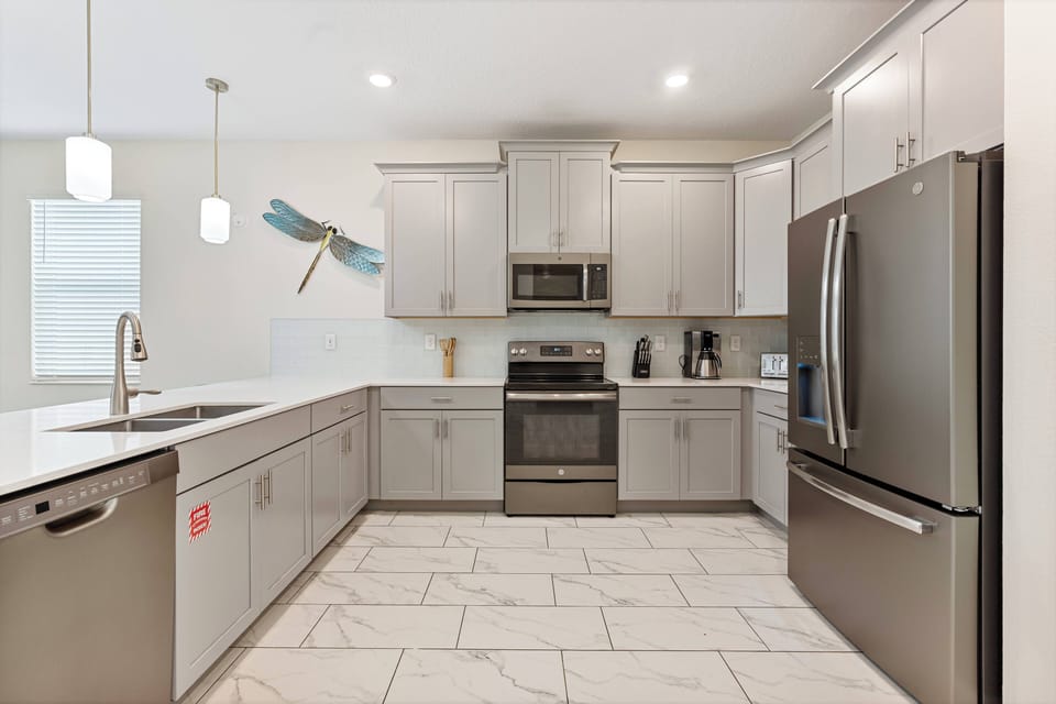 Step into this stylish kitchen featuring sleek stainless steel appliances and light gray cabinetry that complements the bright, open layout. The elegant tile flooring adds a touch of sophistication, making meal prep a delight.