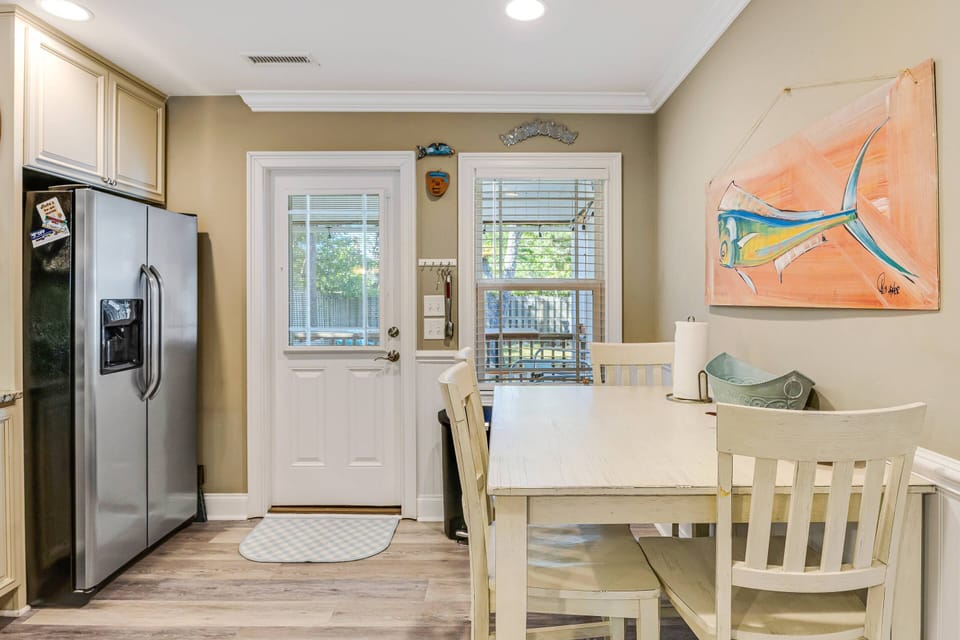Simple, welcoming, and easy living. Bright kitchen-dining nook: white table, stainless fridge, sunny window, coastal art.