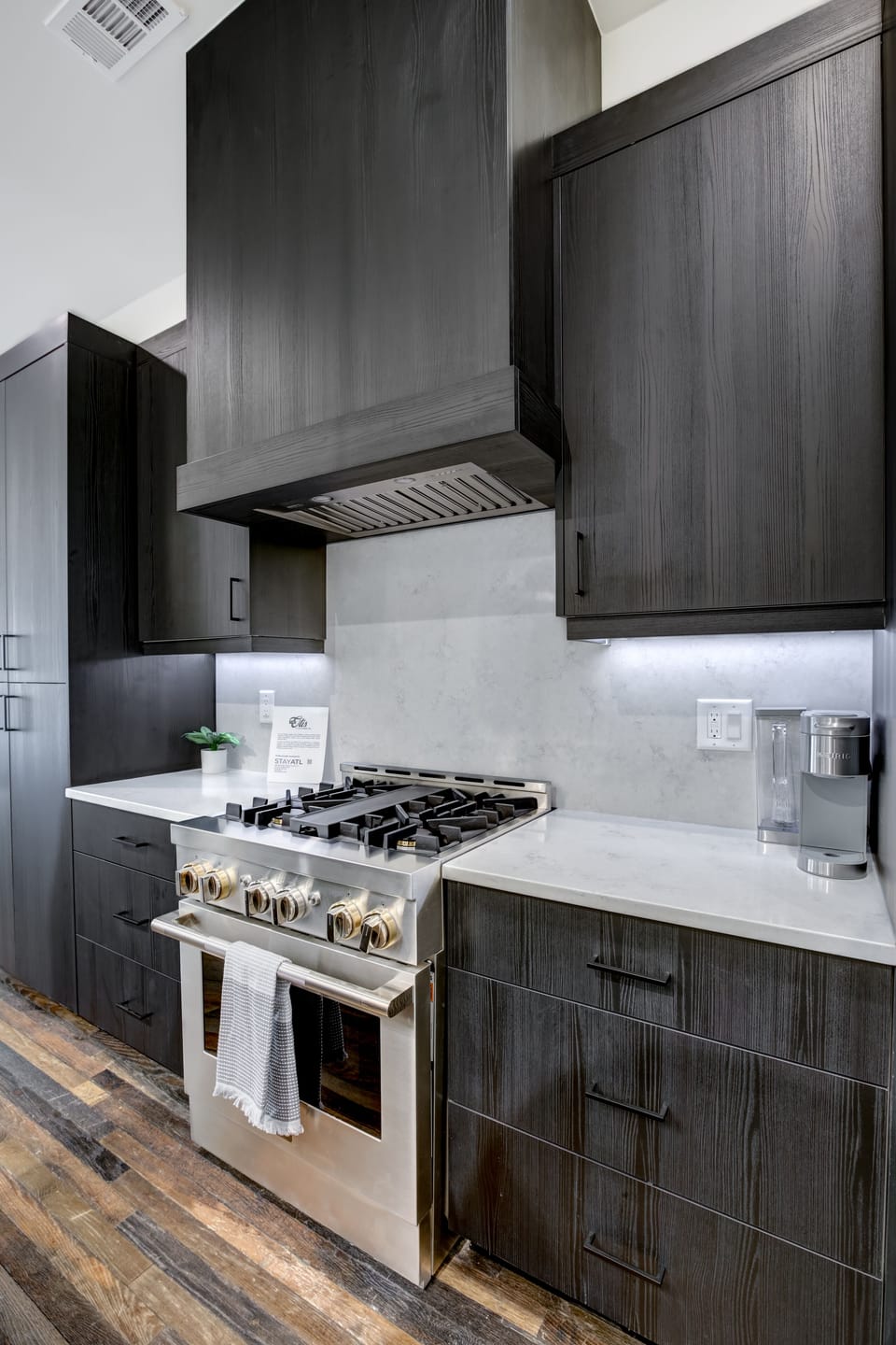 Contemporary kitchen corner w/ gas stove, vent hood & clean marble surfaces