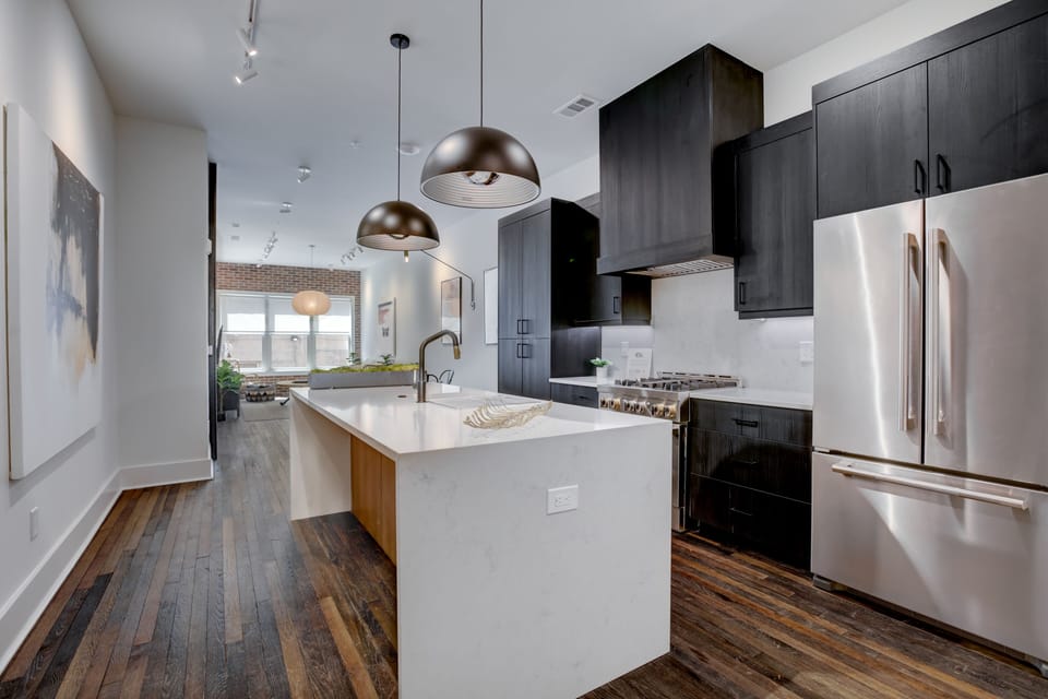 Sleek kitchen w/ large island, pendant lighting & dark cabinetry for a modern feel