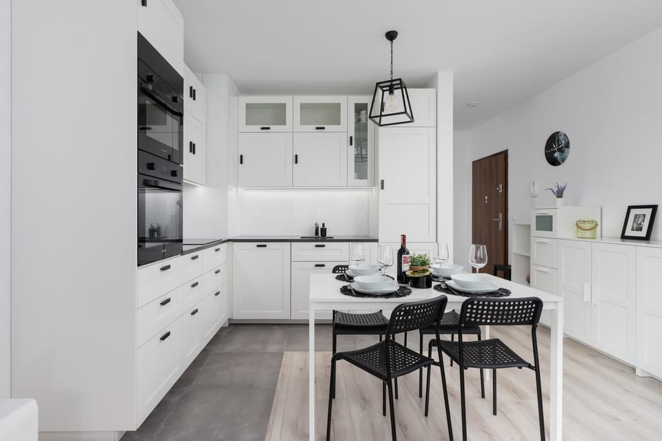 A modern kitchen with white cabinetry, a black dining table, and pendant lighting. The open layout seamlessly connects with the living area.
