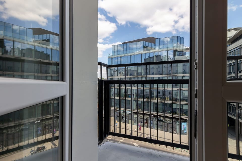 A balcony overlooking the city, with a view of urban buildings and bright skies.