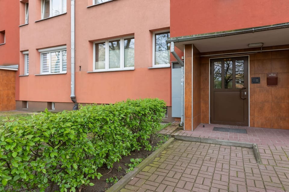 The entrance to the building, featuring a red facade and a tidy pathway surrounded by greenery.

