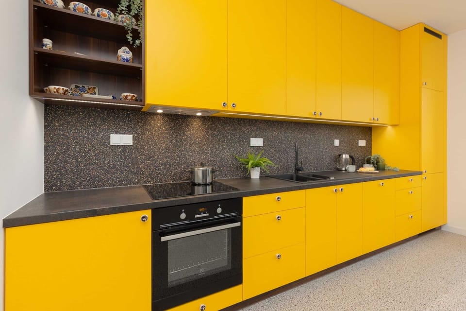 Kitchen featuring bold yellow cabinets, a sleek black backsplash, and modern kitchen essentials.
