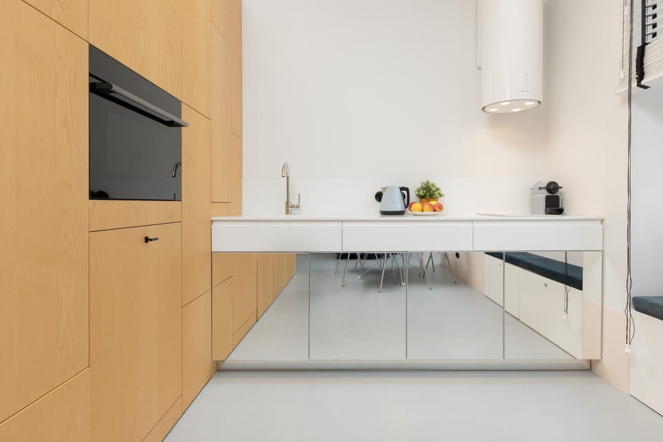 Modern kitchen with white countertops, wooden cabinetry, and a built-in oven, offering a sleek and functional design.
