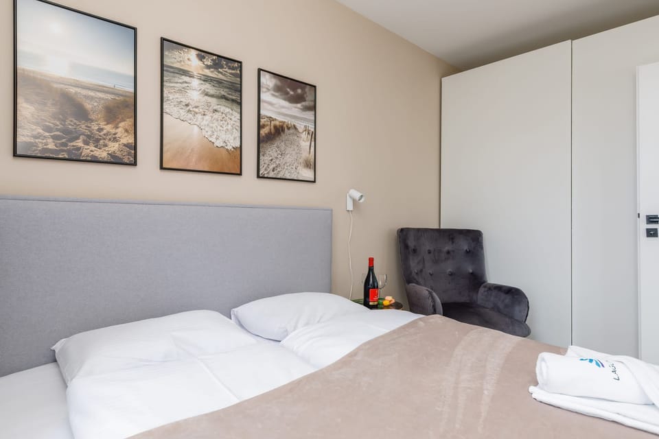 Another bedroom featuring a double bed with white linens, a small black armchair, and framed artwork on the wall. The color palette is neutral and calming.