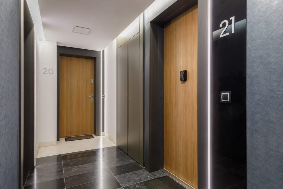 A hallway inside the apartment complex, featuring elegant wooden doors and sleek black flooring. The area appears clean and modern.