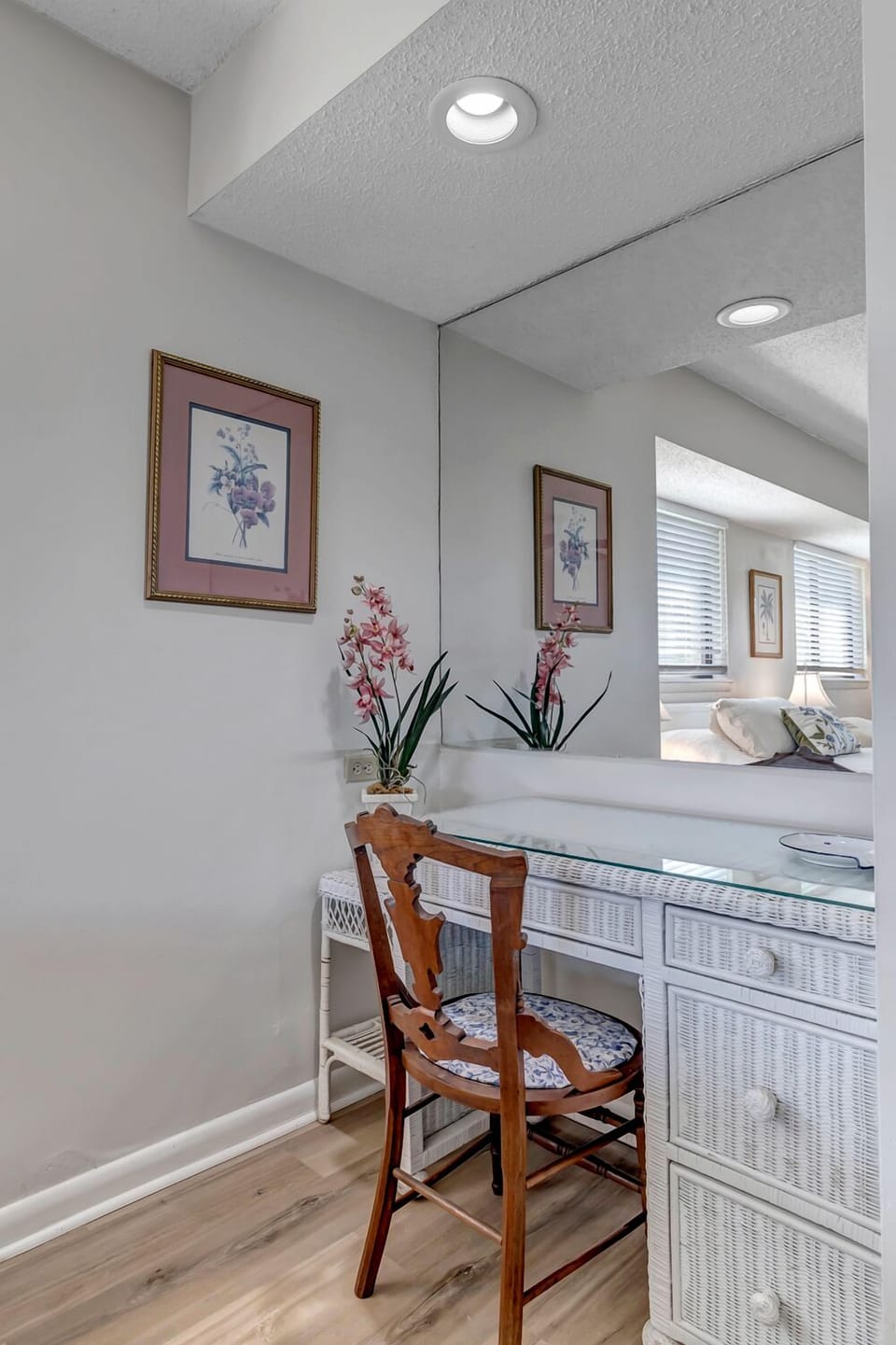 - Chic white wicker desk with a glass top and cushioned wooden chair setup
- Framed floral art and mirrored wall add charm and reflective light
- Ideal corner for work, writing, or getting ready for a night out