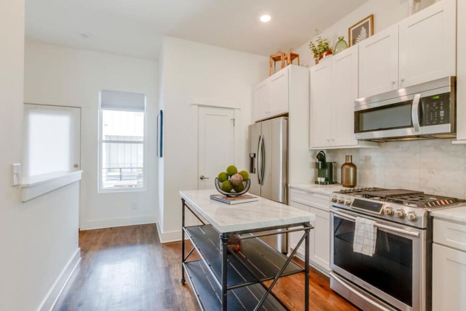 Kitchen with white cabinetry, gas range, stainless appliances, island, and dark wood floors