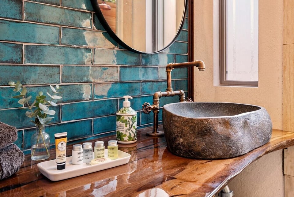 Stone vessel sink, copper pipe fixtures, and teal tile. Toiletries by Thena Pure included.