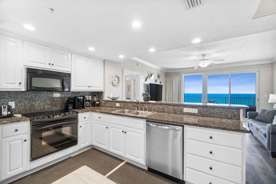 Bright kitchen w/ white cabinets, modern appliances & a glimpse of the water beyond.