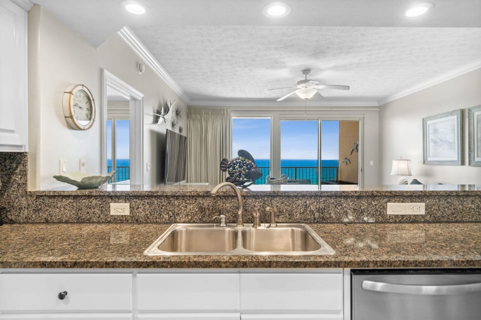 Spacious kitchen w/ granite countertops, sink & plenty of prep space under a ceiling fan.