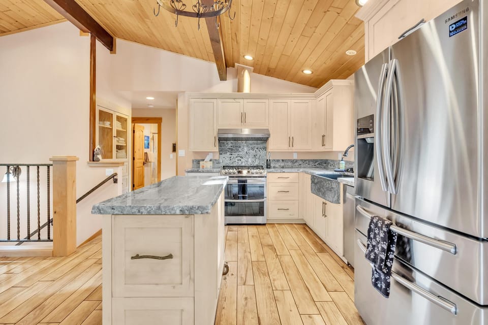 Kitchen with light wood cabinetry, granite counters, farmhouse sink, stainless steel appliances, and vaulted pine ceiling.