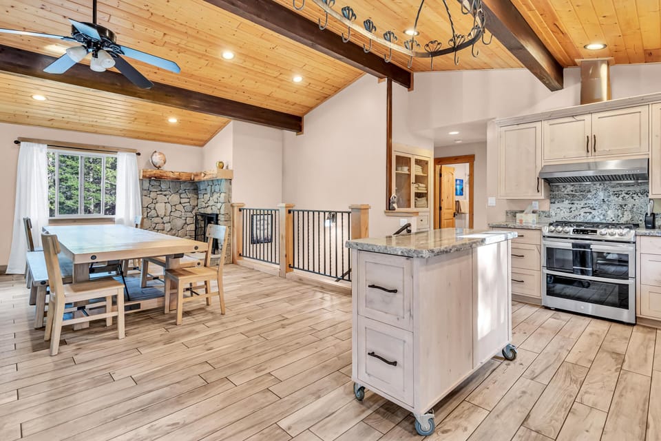 Dining area with light wood table and bench seating beside a stone fireplace under pine-paneled vaulted ceiling.
