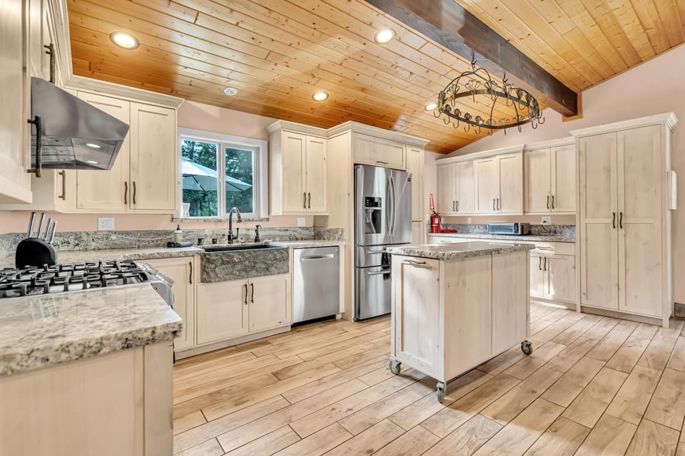 Kitchen features granite countertops, farmhouse sink, stainless steel appliances, and a wood-paneled vaulted ceiling.