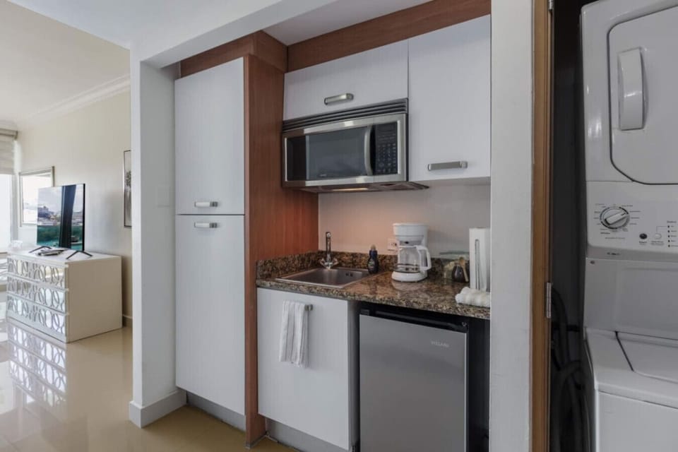 compact kitchen area with microwave, coffee maker, and mini fridge next to a stacked washer and dryer