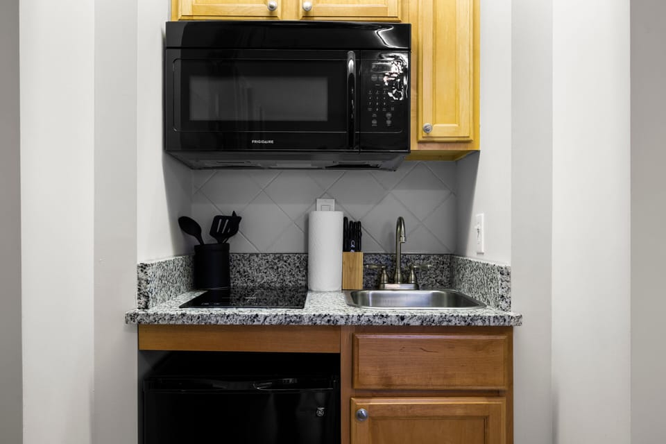 A compact kitchen equipped with a sink, mini fridge, microwave, coffee maker, toaster, and stove and dishes utensils