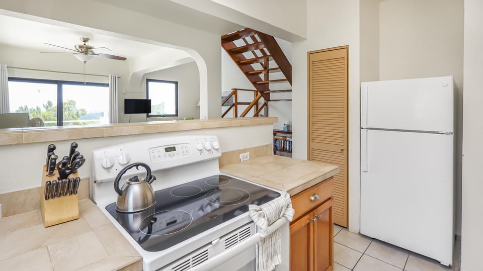 Tile countertops surround the white electric stove with a stainless steel kettle and knife block nearby.