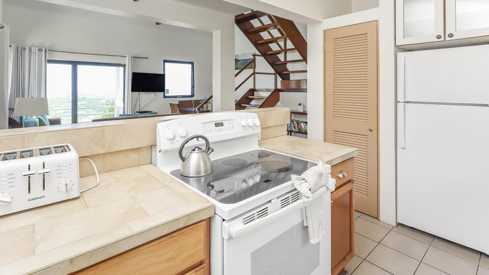 Tile countertops surround the white electric stove and toaster in the bright kitchen with wooden cabinets.