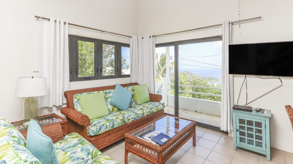Wicker sofas with tropical cushions face a glass-top coffee table beside sliding doors opening to a balcony view.