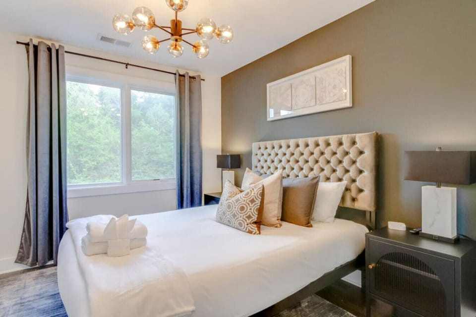 Bedroom with tufted headboard, sputnik chandelier, framed art above bed, and window with green view